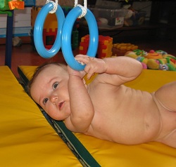 Держась за подвешенные к спорткомплексу кольца, малыш будет пытаться сесть или перевернуться. При этом развивает мелкую моторику и координацию движений